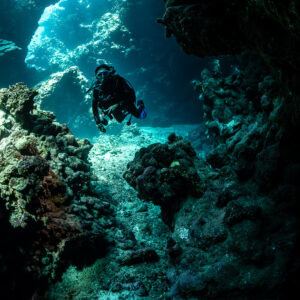 Diver descending through cave toward sandy floor, vertical, Shaab Claudio, Red Sea, Egypt