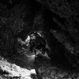 Black and white image of diver with torch inside cave, vertical, Shaab Claudio, Red Sea, Egypt