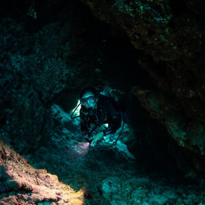 Diver lighting cave wall with torch in darkness, vertical, Shaab Claudio, Red Sea, Egypt
