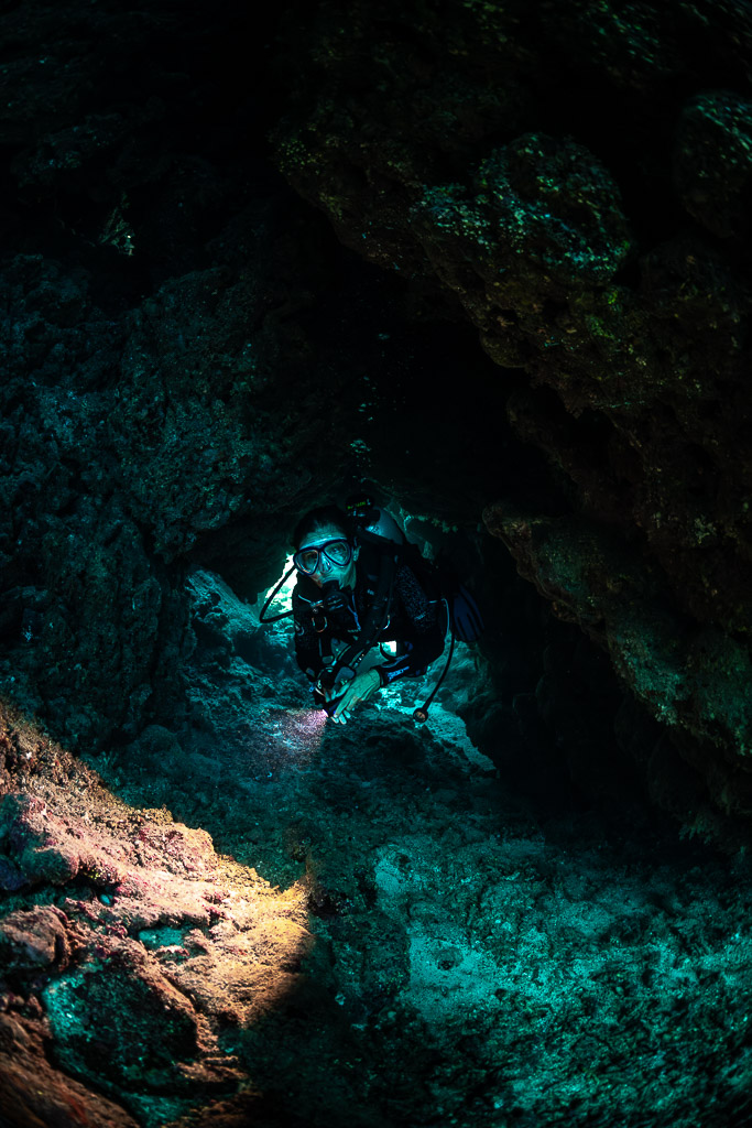 Diver lighting cave wall with torch in darkness, vertical, Shaab Claudio, Red Sea, Egypt