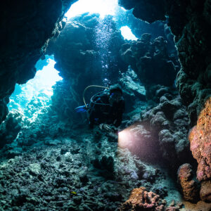 Diver with torch in cave beside orange encrusted boulder, Shaab Claudio, Red Sea, Egypt