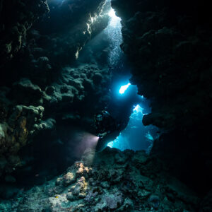 Diver with torch under multiple cave skylights, vertical, Shaab Claudio, Red Sea, Egypt