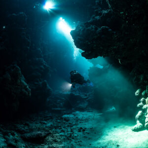 Diagonal light shafts falling on diver in cave, vertical, Shaab Claudio, Red Sea, Egypt