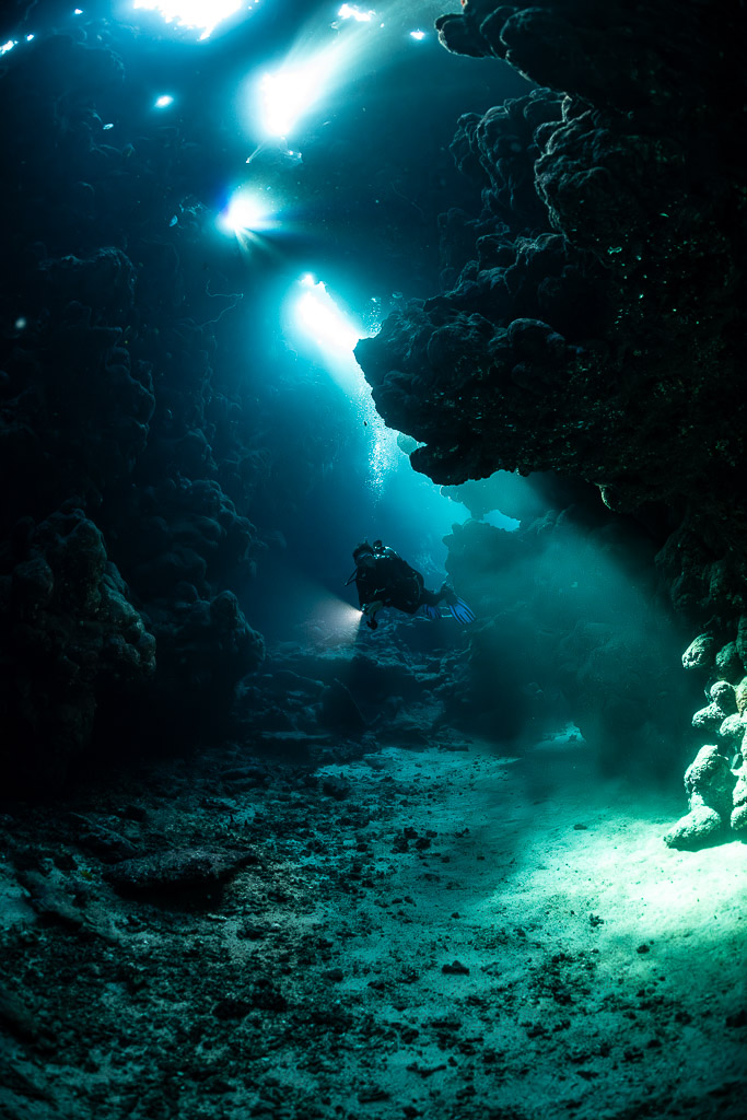Diagonal light shafts falling on diver in cave, vertical, Shaab Claudio, Red Sea, Egypt