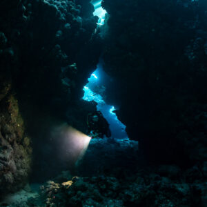 Diver with torch in narrow cave fissure, vertical, Shaab Claudio, Red Sea, Egypt
