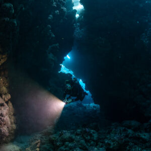 Diver lighting the way in narrow cave fissure, closer vertical, Shaab Claudio, Red Sea, Egypt