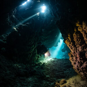 Torch beams crossing in dark cave with blue exit, vertical, Shaab Claudio, Red Sea, Egypt