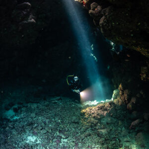 Rai de lumière unique frappant un plongeur avec phare dans la grotte, Shaab Claudio, mer Rouge, Égypte