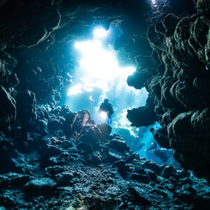 Diver silhouetted against bright cave exit, Shaab Claudio, Red Sea, Egypt