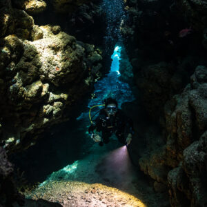 Diver in fissure with torch lighting sandy floor, vertical, Shaab Claudio, Red Sea, Egypt