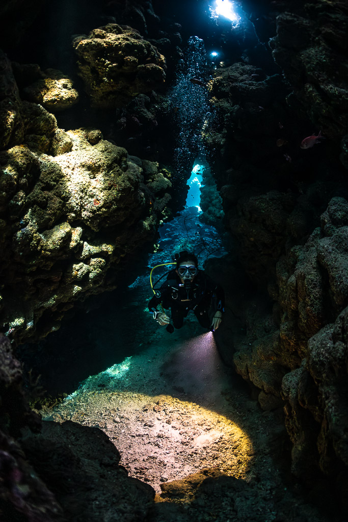 Diver in fissure with torch lighting sandy floor, vertical, Shaab Claudio, Red Sea, Egypt