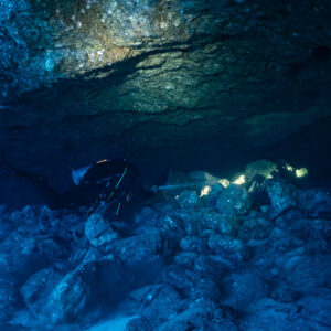 Divers with torches exploring a low underwater cave over a boulder floor, Roca O'Neal (Socorro), Revillagigedo, Mexico