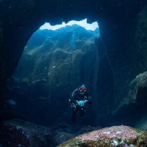 Diver beneath a rocky arch with light filtering through the opening, vertical, Roca O'Neal (Socorro), Revillagigedo, Mexico