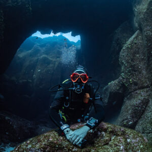 Diver posing on a boulder in front of an underwater arch, vertical, Roca O'Neal (Socorro), Revillagigedo, Mexico