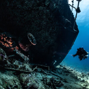 Diver silhouetted beside the dark hull of the wreck, Al Kahfain wreck, Red Sea, Egypt