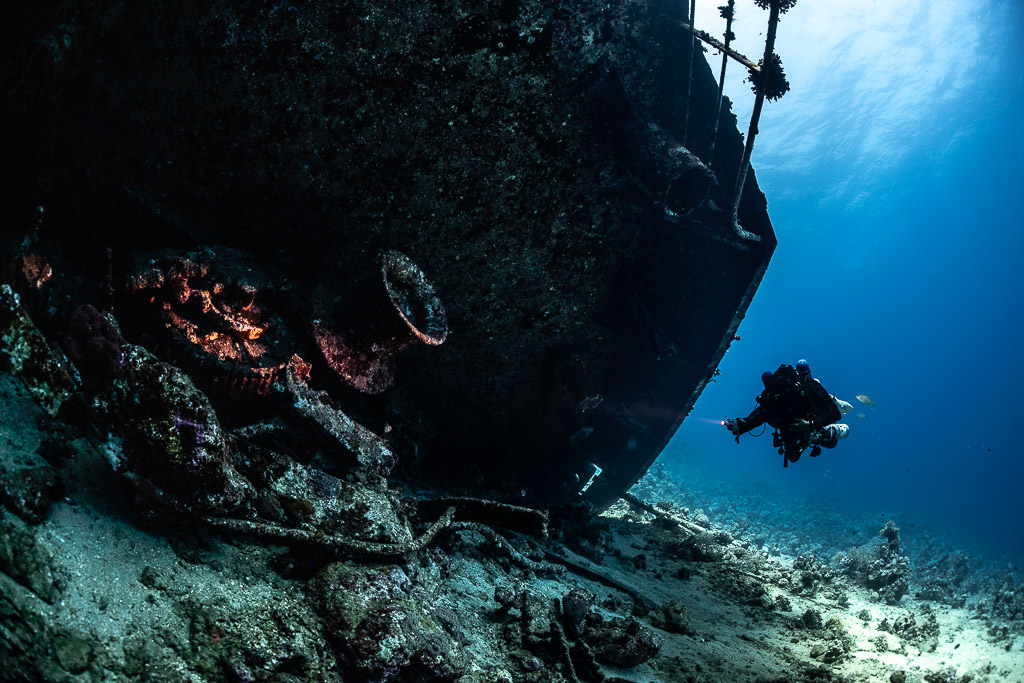 Diver silhouetted beside the dark hull of the wreck, Al Kahfain wreck, Red Sea, Egypt