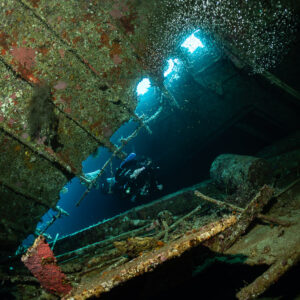 Diver lit by sunbeams through openings of the wreck, Al Kahfain wreck, Red Sea, Egypt