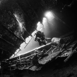 Black-and-white diver under light shafts inside the wreck, Al Kahfain wreck, Red Sea, Egypt