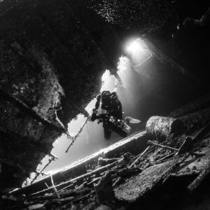 Black-and-white diver backlit by openings inside the wreck, Al Kahfain wreck, Red Sea, Egypt