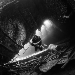 Black-and-white diver near collapsed structure under light beams, Al Kahfain wreck, Red Sea, Egypt