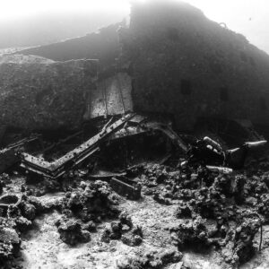 Black-and-white collapsed wreckage with diver at the hull base, Al Kahfain wreck, Red Sea, Egypt