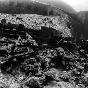 Black-and-white wreck side with windows and debris, diver at right, Al Kahfain wreck, Red Sea, Egypt