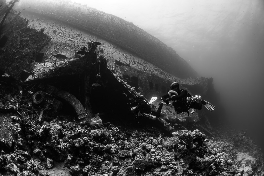 Black-and-white pair of divers at a collapsed wreck section, Al Kahfain wreck, Red Sea, Egypt