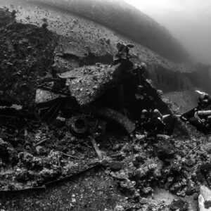 Black-and-white divers with cameras beside wreck debris, Al Kahfain wreck, Red Sea, Egypt