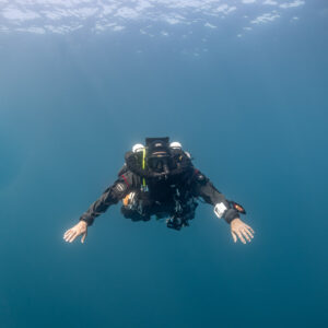 Rebreather diver ascending in blue water, arms spread wide, Chalutier à Benoît wreck (Lacanau), Gironde, France